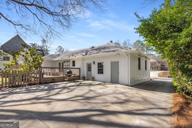 back of house featuring concrete driveway, brick siding, and fence