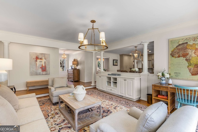 living area with ornate columns, light wood-style flooring, crown molding, and an inviting chandelier