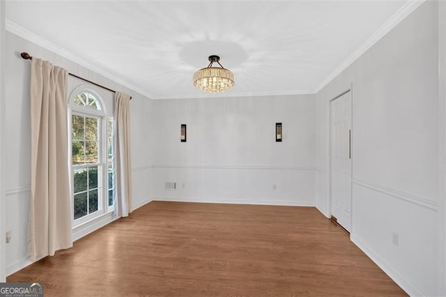 unfurnished room with a notable chandelier, baseboards, wood finished floors, and crown molding