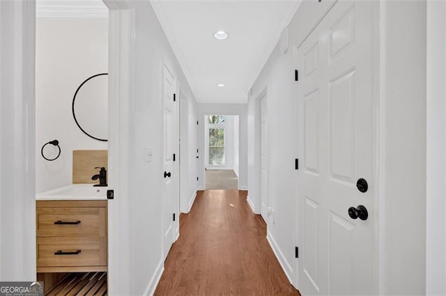 corridor featuring crown molding, a sink, baseboards, and wood finished floors