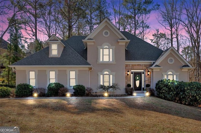 view of front of property with stone siding, a front yard, stucco siding, and roof with shingles