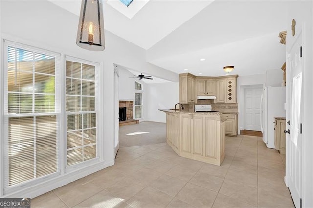 kitchen with stove, freestanding refrigerator, a stone fireplace, vaulted ceiling with skylight, and under cabinet range hood