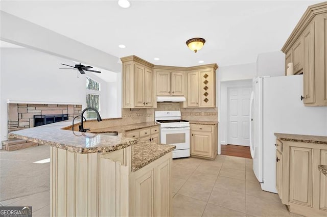 kitchen featuring a sink, a peninsula, under cabinet range hood, white appliances, and cream cabinetry