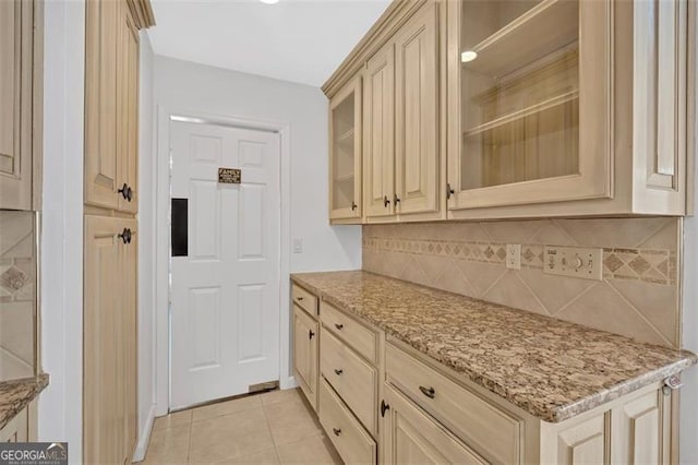 kitchen featuring tasteful backsplash, glass insert cabinets, light stone counters, and light tile patterned flooring