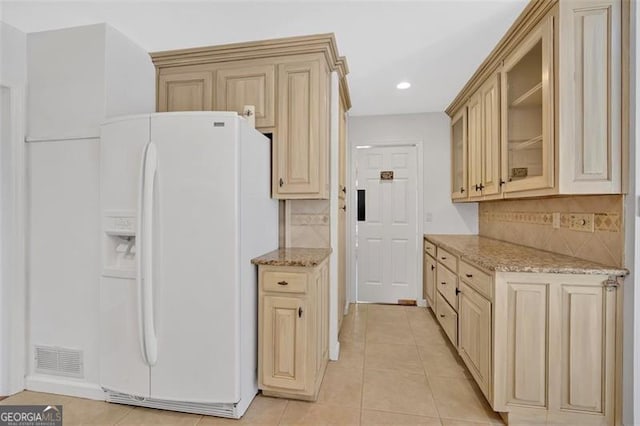 kitchen featuring light tile patterned floors, light stone counters, visible vents, white fridge with ice dispenser, and glass insert cabinets