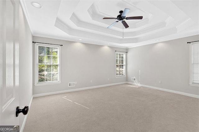 carpeted empty room featuring a raised ceiling, visible vents, ornamental molding, ceiling fan, and baseboards