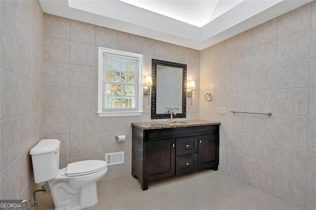 bathroom with toilet, tile patterned flooring, visible vents, and tile walls