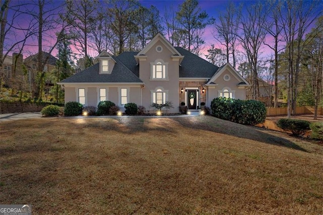 view of front facade featuring a shingled roof, stucco siding, and a yard