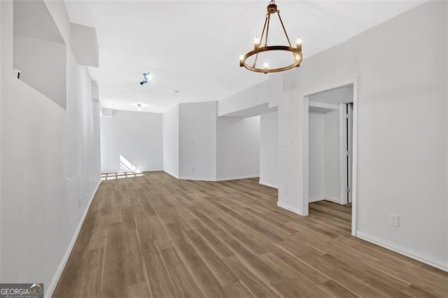 spare room with a chandelier, wood finished floors, visible vents, and baseboards