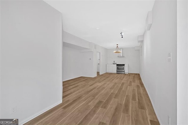 unfurnished living room featuring light wood-style flooring, a chandelier, and baseboards