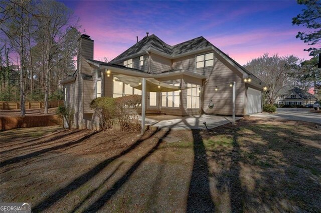 view of front of house featuring driveway, a chimney, fence, an attached garage, and a patio