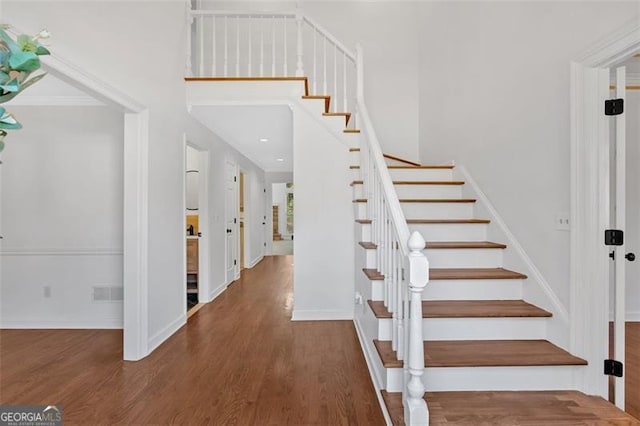 stairway with baseboards, a high ceiling, visible vents, and wood finished floors