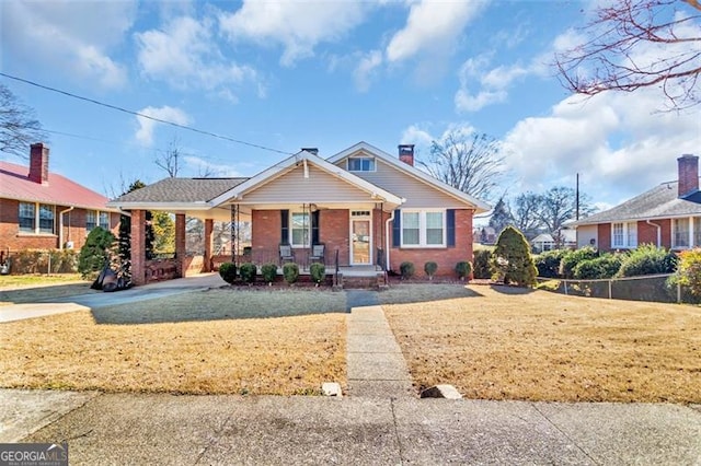 bungalow featuring brick siding, covered porch, a carport, driveway, and a front lawn