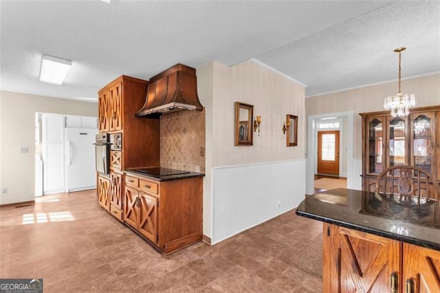 kitchen featuring pendant lighting, brown cabinets, backsplash, an inviting chandelier, and stainless steel oven