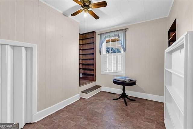 interior space featuring built in shelves, crown molding, wood walls, ceiling fan, and baseboards