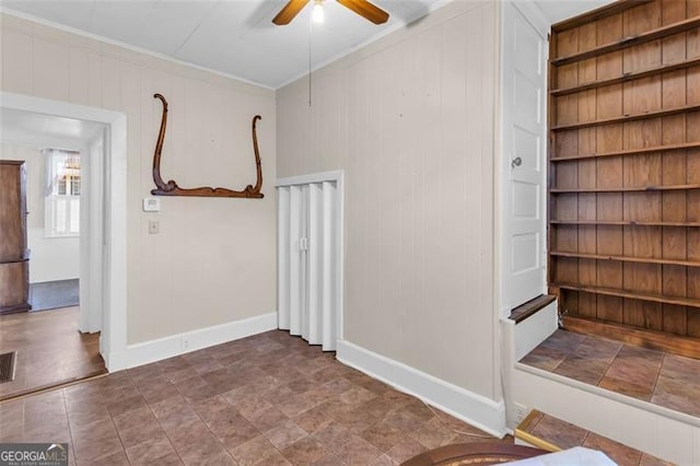 unfurnished room featuring baseboards, ceiling fan, ornamental molding, wood walls, and built in shelves