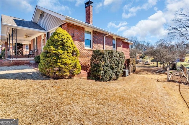 view of property exterior with brick siding, a yard, a chimney, a ceiling fan, and cooling unit