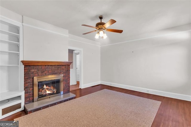 unfurnished living room featuring wood finished floors, a ceiling fan, built in features, baseboards, and a brick fireplace