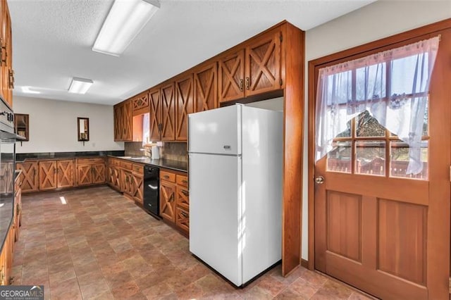 kitchen with brown cabinetry, freestanding refrigerator, a sink, and dark countertops