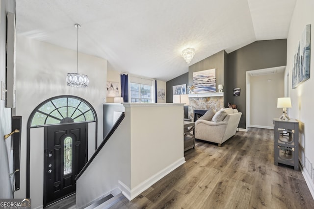 entrance foyer with a chandelier, lofted ceiling, a stone fireplace, wood finished floors, and baseboards