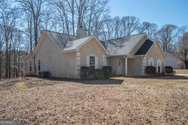 view of side of property with roof with shingles, a chimney, stucco siding, and central air condition unit