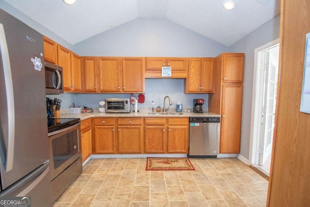 kitchen featuring brown cabinets, a toaster, lofted ceiling, appliances with stainless steel finishes, and a sink