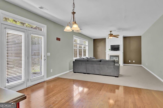 living room featuring ceiling fan, baseboards, wood finished floors, and a glass covered fireplace