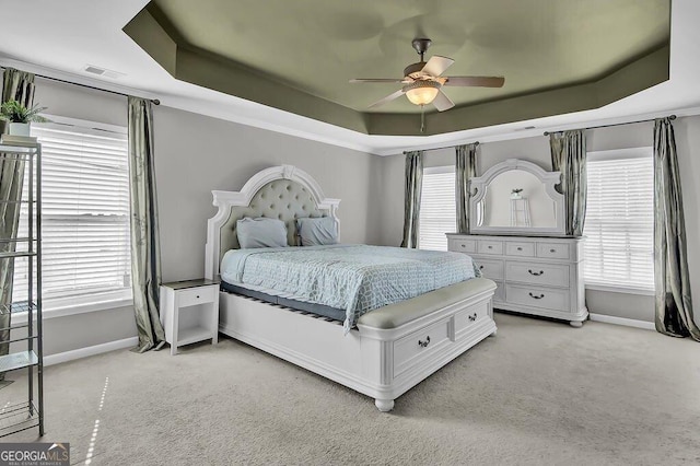 bedroom with visible vents, a tray ceiling, baseboards, and light colored carpet