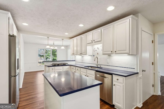 kitchen featuring dark wood finished floors, dark countertops, appliances with stainless steel finishes, a peninsula, and a sink