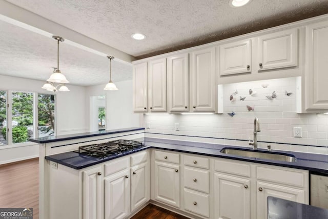 kitchen with a peninsula, black gas cooktop, dark countertops, and a sink