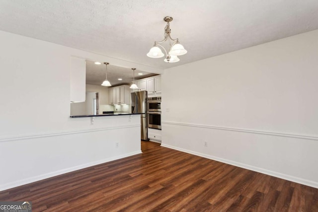 unfurnished living room with a chandelier, dark wood-style flooring, a textured ceiling, and baseboards