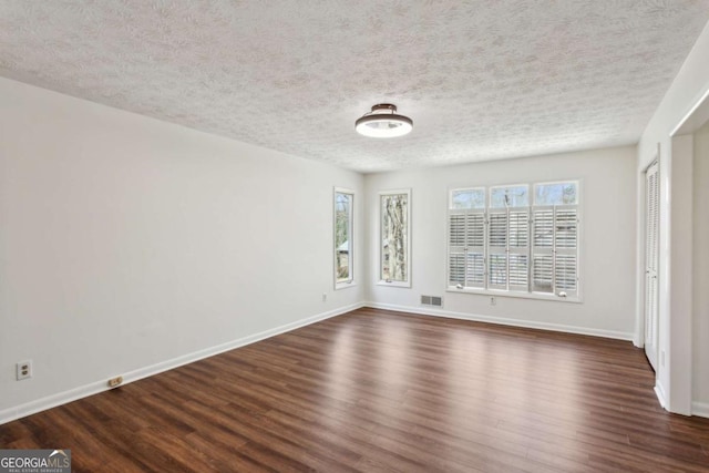 spare room featuring visible vents, dark wood finished floors, and baseboards