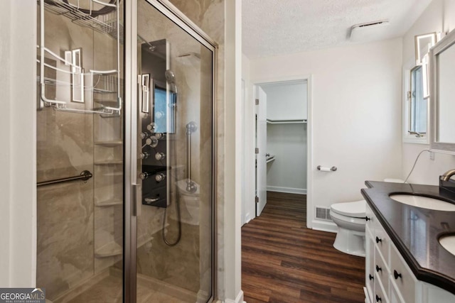 bathroom featuring a walk in closet, a stall shower, vanity, a textured ceiling, and wood finished floors