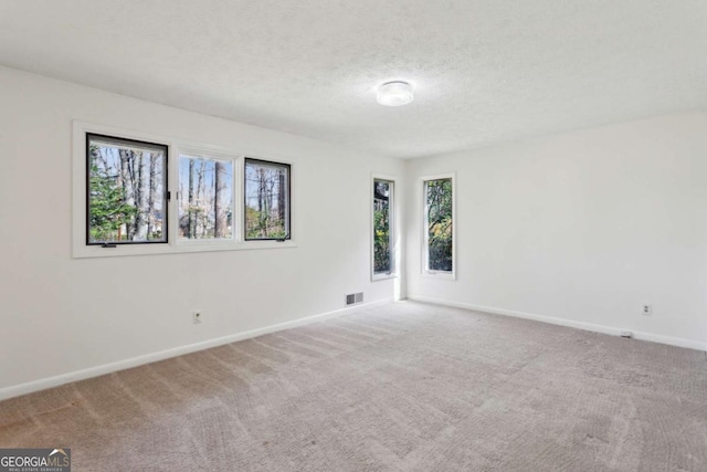 empty room featuring visible vents, carpet flooring, a textured ceiling, and baseboards