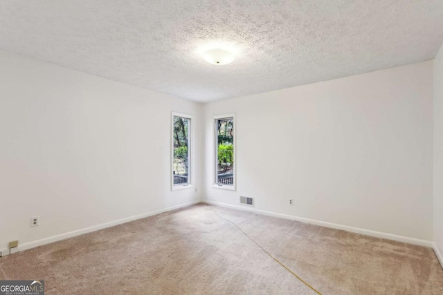 carpeted empty room featuring a textured ceiling, visible vents, and baseboards