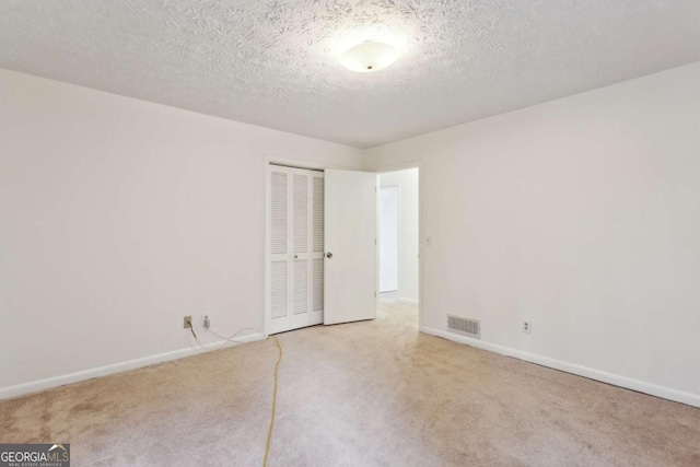 carpeted spare room with a textured ceiling, visible vents, and baseboards