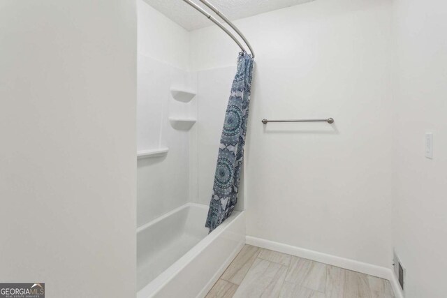 full bath with a textured ceiling, wood finished floors, visible vents, baseboards, and shower / bath combo with shower curtain