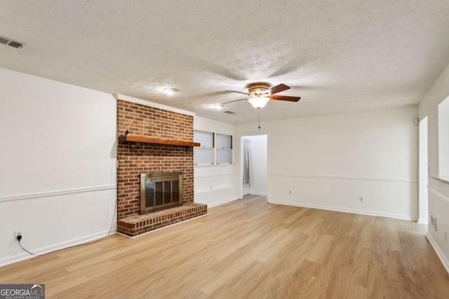 unfurnished living room featuring a brick fireplace, visible vents, light wood-style flooring, and a textured ceiling