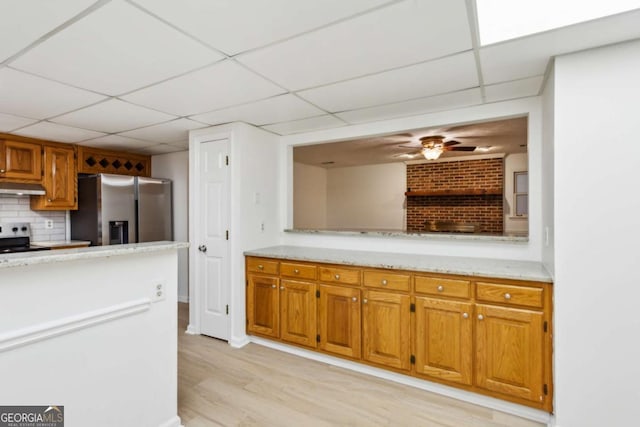 kitchen with stainless steel fridge, electric range, brown cabinetry, light wood-style floors, and under cabinet range hood