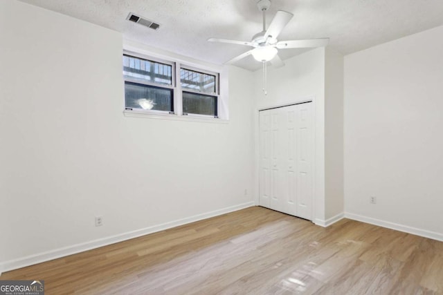 unfurnished bedroom featuring a textured ceiling, wood finished floors, visible vents, baseboards, and a closet