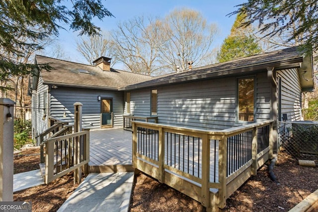 rear view of house featuring a chimney, roof with shingles, and a deck