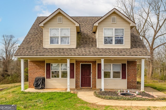 view of front of property with covered porch, roof with shingles, a front yard, and brick siding