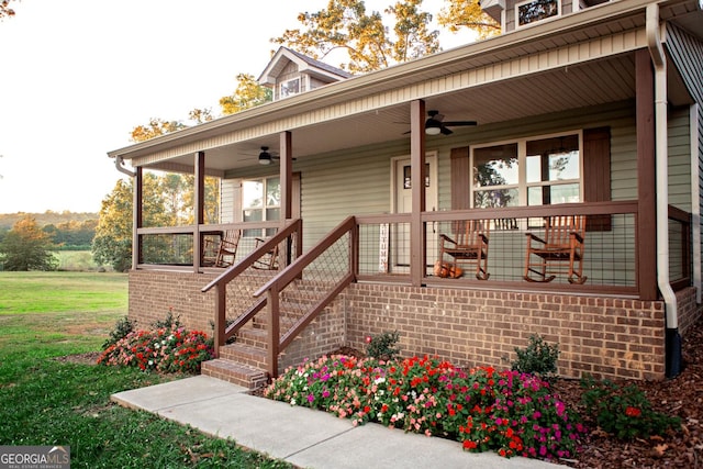 view of exterior entry featuring brick siding, a yard, a porch, and a ceiling fan