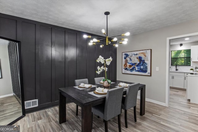 dining area with visible vents, a notable chandelier, light wood-style flooring, and a textured ceiling