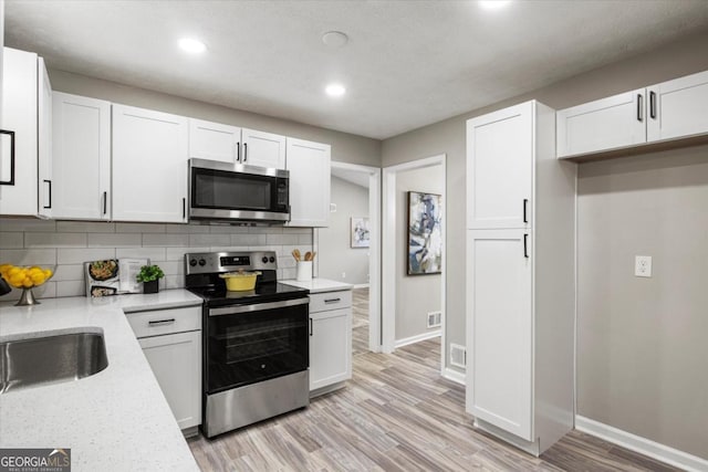 kitchen featuring stainless steel appliances, white cabinetry, baseboards, light wood-style floors, and backsplash