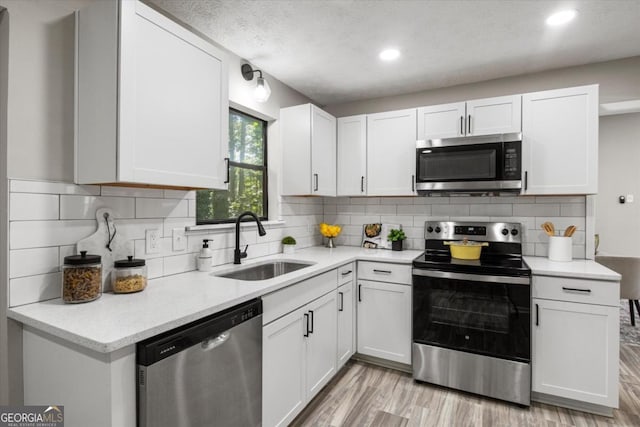 kitchen with white cabinets, light wood finished floors, stainless steel appliances, and a sink