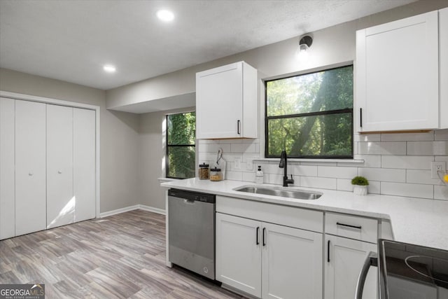 kitchen featuring a sink, white cabinetry, light countertops, stainless steel dishwasher, and decorative backsplash