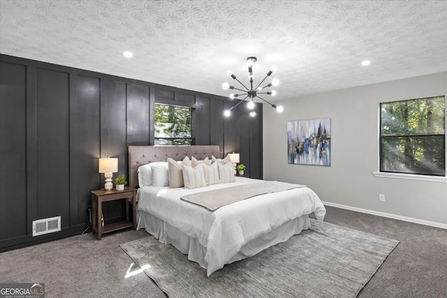 bedroom with visible vents, an inviting chandelier, a textured ceiling, carpet floors, and a decorative wall