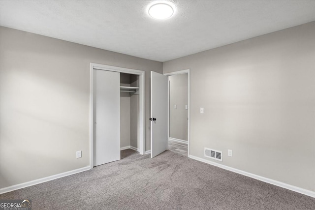 unfurnished bedroom featuring carpet floors, a closet, visible vents, a textured ceiling, and baseboards