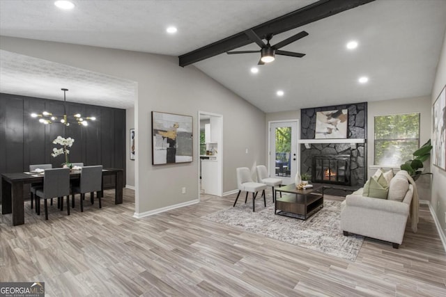 living room with vaulted ceiling with beams, light wood-type flooring, a stone fireplace, and plenty of natural light